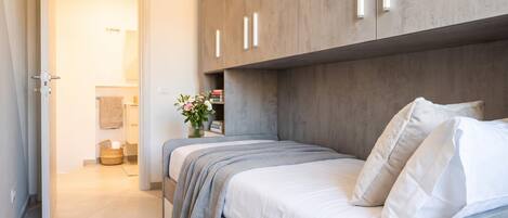 Ein Schlafzimmer mit Bett, Nachttisch, Kleiderschrank und einem durchgegangenen Tür sichtbaren Badezimmer.