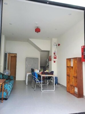 A room with a dining table, chairs, a sofa, a wooden cabinet, and a red fire alarm. - D Global Studio (Ngu Hanh Son)