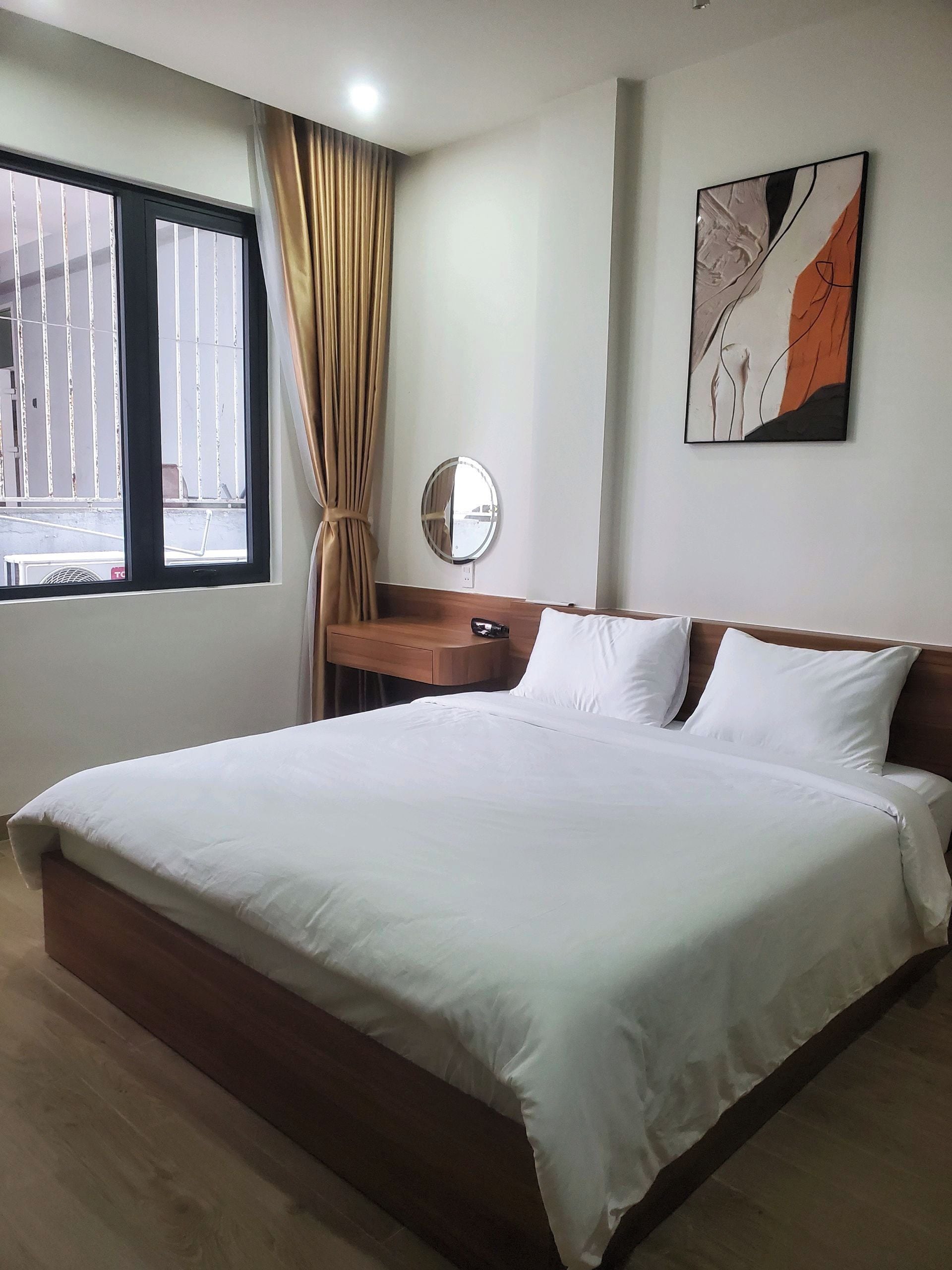 Une chambre d’hôtel avec un grand lit, une table de chevet, un miroir et une fenêtre avec des rideaux.