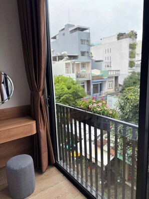 A balcony with a metal railing, a potted plant with pink flowers, and a view of surrounding buildings. - D Global Studio (Ngu Hanh Son)