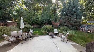 A patio area with a concrete floor, surrounded by greenery and a wooden fence.