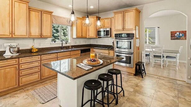 Une cuisine moderne avec des meubles en bois, un îlot central doté de tabourets, des appareils en acier inoxydable et un éclairage suspendu.