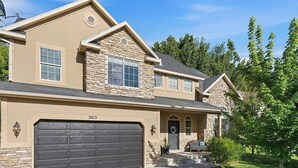 Une maison à deux étages avec un garage, une façade en pierre et une pelouse bien entretenue.