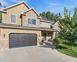 A two-story house with a garage, stone facade, and a well-maintained lawn. - Parkside 4-BR – Game Room, Waffles, Pets OK (Orem)