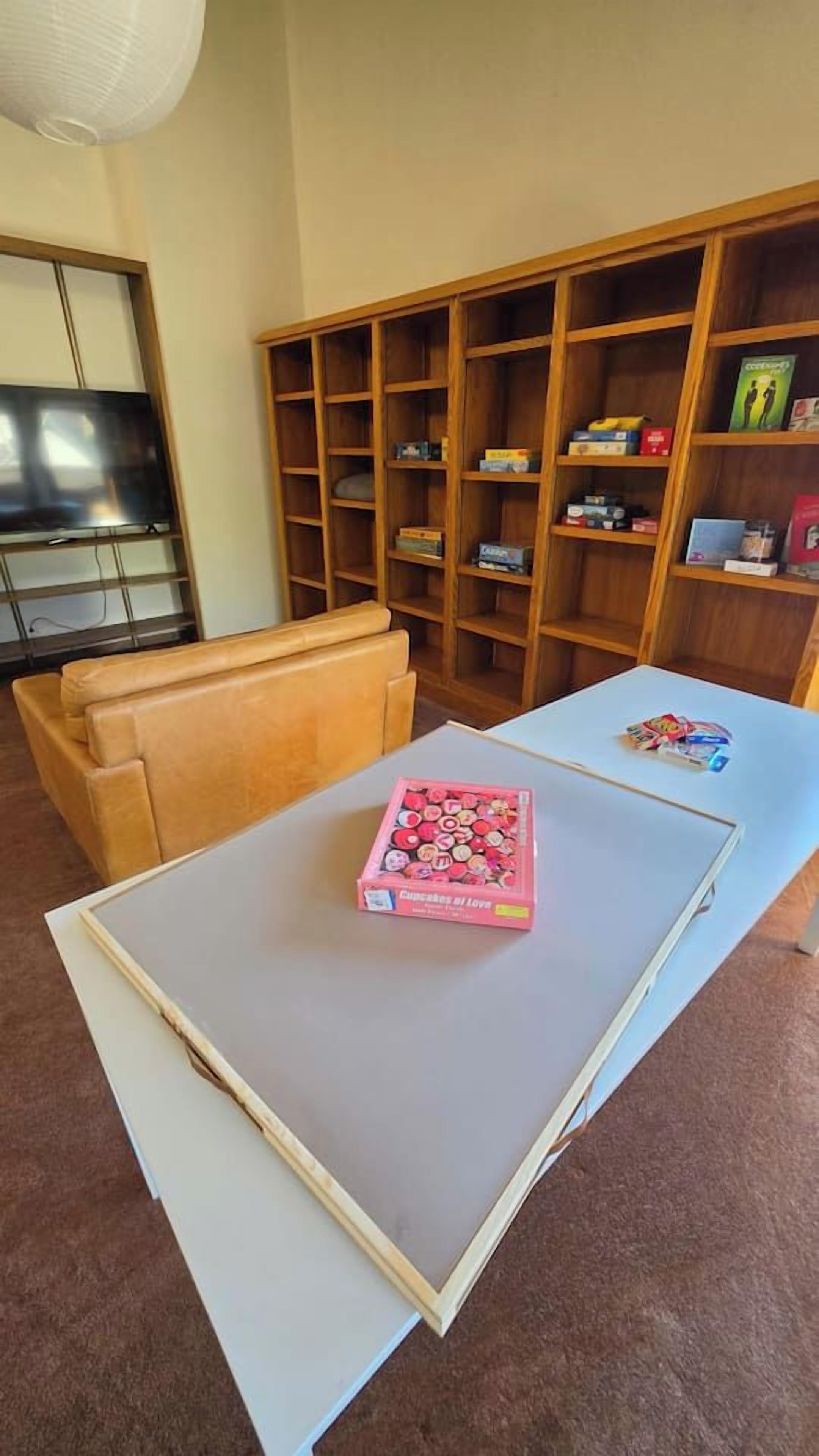 A living room with a sofa, a coffee table with a box of chocolates, and a bookshelf with various items.