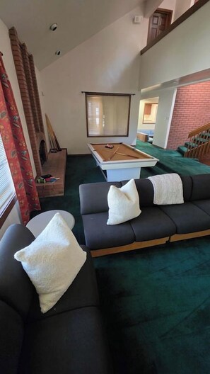 A living room with a pool table, a sofa with cushions, and a fireplace.