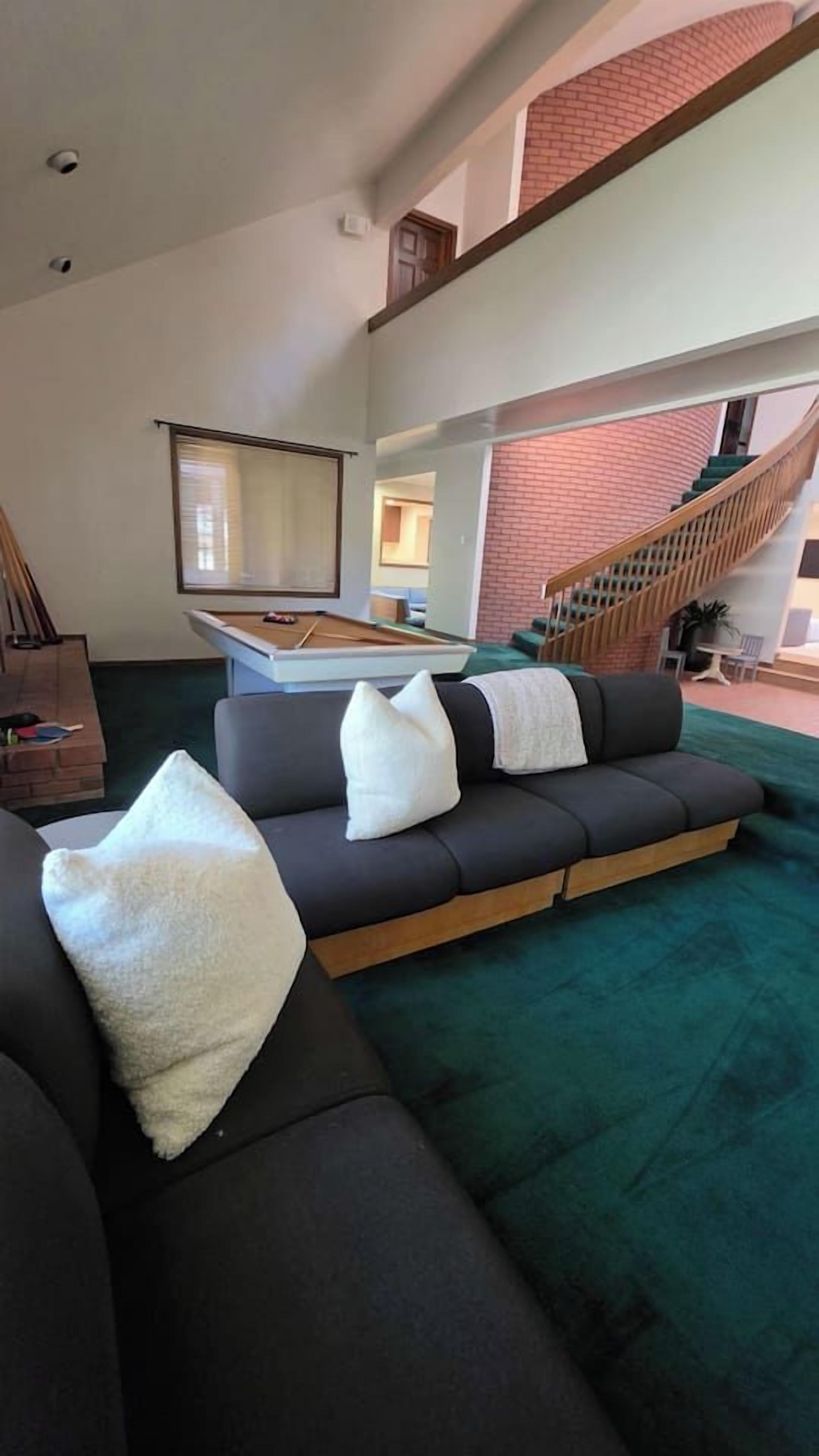 Un salon avec une table de billard, un canapé et un escalier.