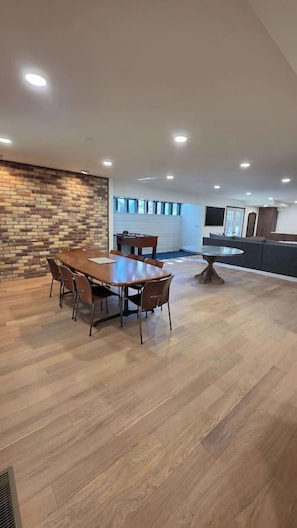 A spacious room with a large wooden dining table, several chairs, a round coffee table, and a brick accent wall.