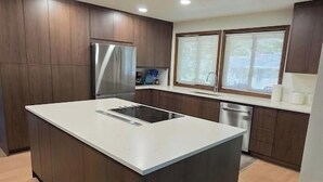 A modern kitchen with a central island, wooden cabinets, stainless steel appliances, and a window providing natural light. - 5-BR Family Retreat – Pool Table & Waffles (Provo)