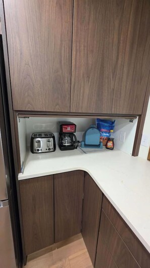 A compact kitchenette with a toaster, coffee maker, and a bag of snacks.