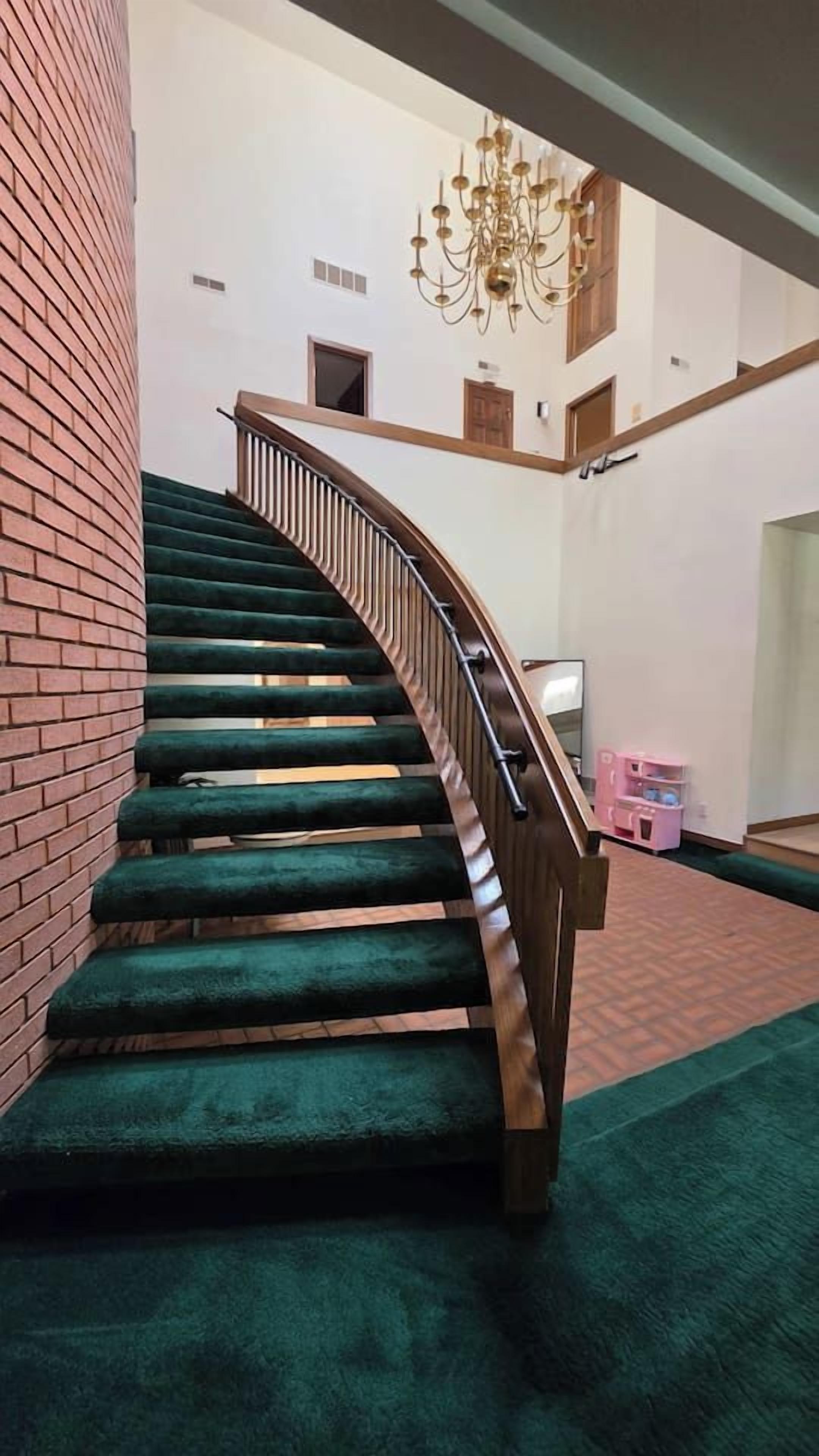 Una escalera de caracol con peldaños cubiertos de moqueta verde y barandilla de madera, que conduce a un piso superior.