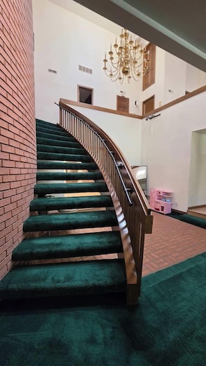 A spiral staircase with green carpeted steps and a wooden handrail, leading to an upper floor.