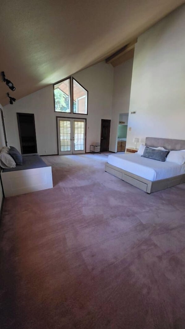 A spacious bedroom with a large bed, a seating area, and a sliding glass door leading to a balcony.