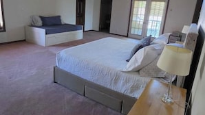 Een slaapkamer met een groot bed, nachtkastje, kapstok en raam.