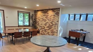 Een ruime kamer met een ronde tafel, een tafelvoetbaltafel en een accentmuur van baksteen.