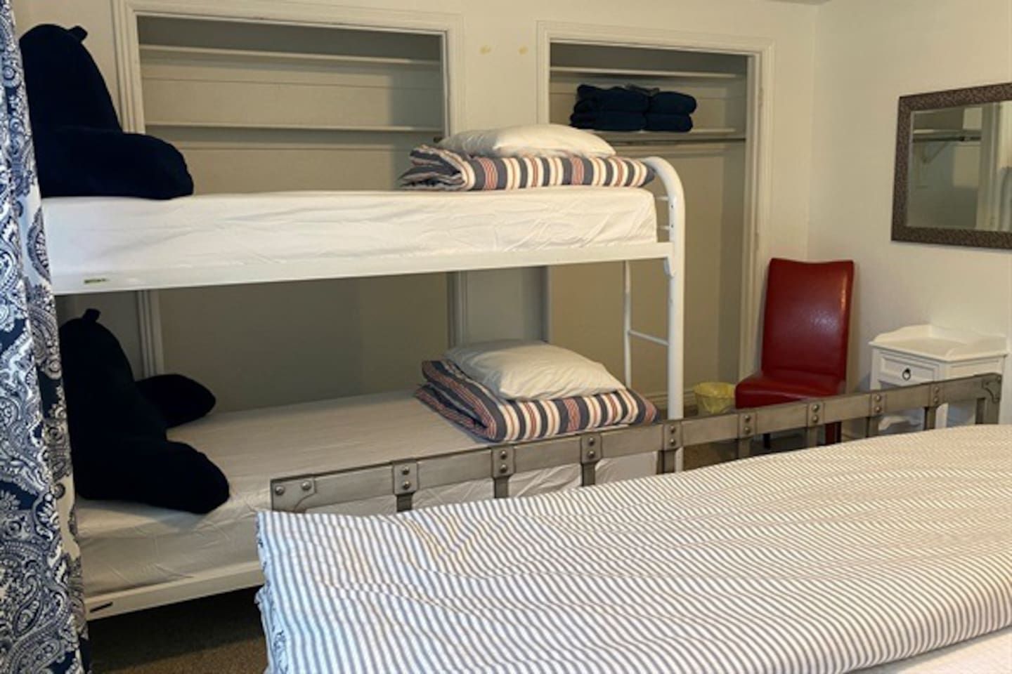 Quarto com beliche, cadeira vermelha, mesa pequena e espelho na parede.