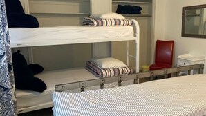 Une chambre avec un lit superposé, composé d’un lit du bas et d’un lit du haut, une chaise rouge, une petite table et un miroir accroché au mur.