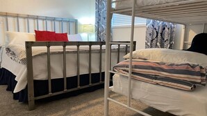 Une chambre avec un lit superposé, dont le lit du bas est accessible, une table de chevet et une lampe.