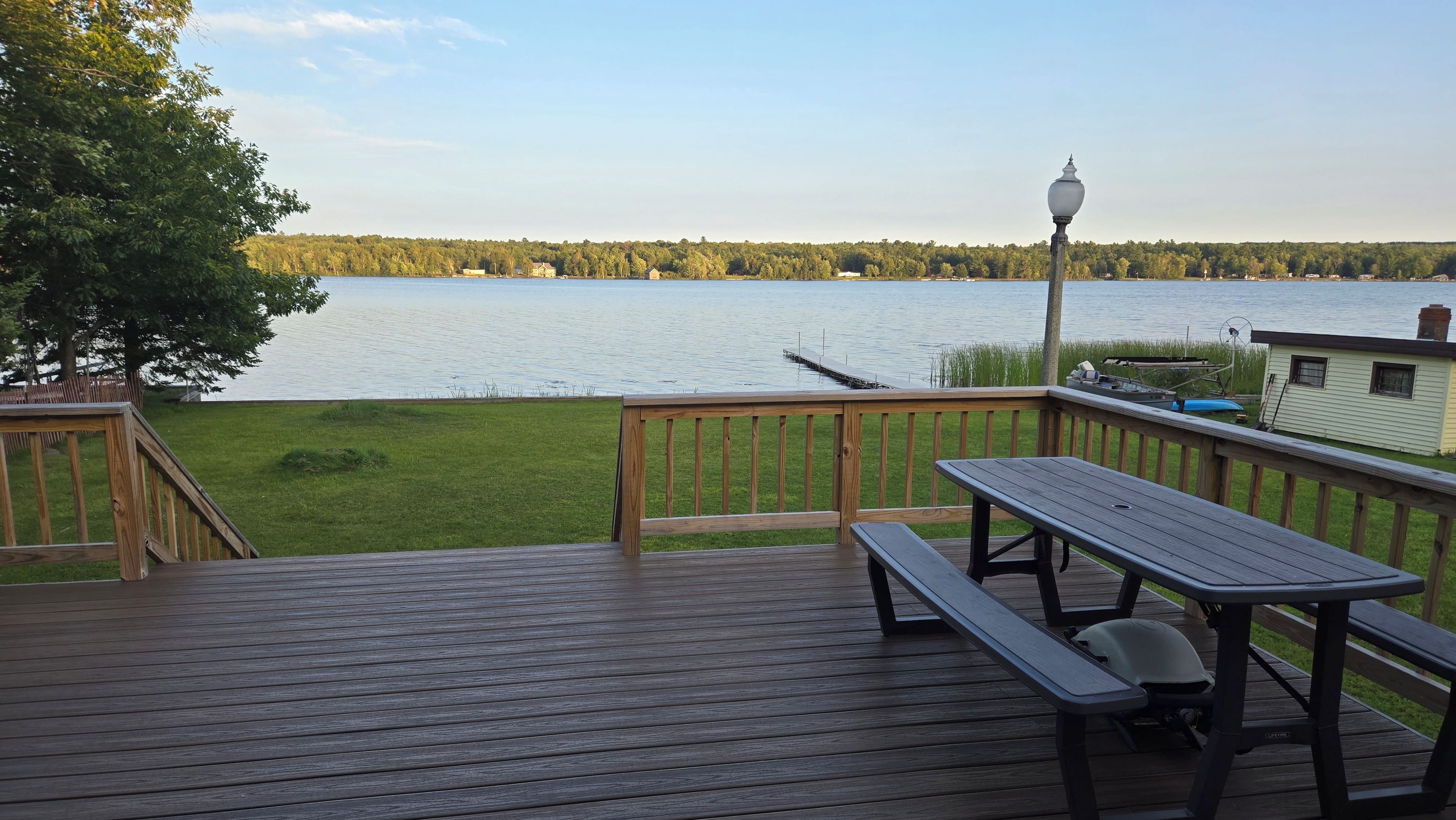 Una terraza de madera con una mesa de picnic y bancos, con vista a un lago.