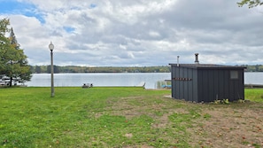A grassy area with a small shed, a picnic table, and a lamp post near a lake. - 3-bedroom • All season lakehouse (Hancock)