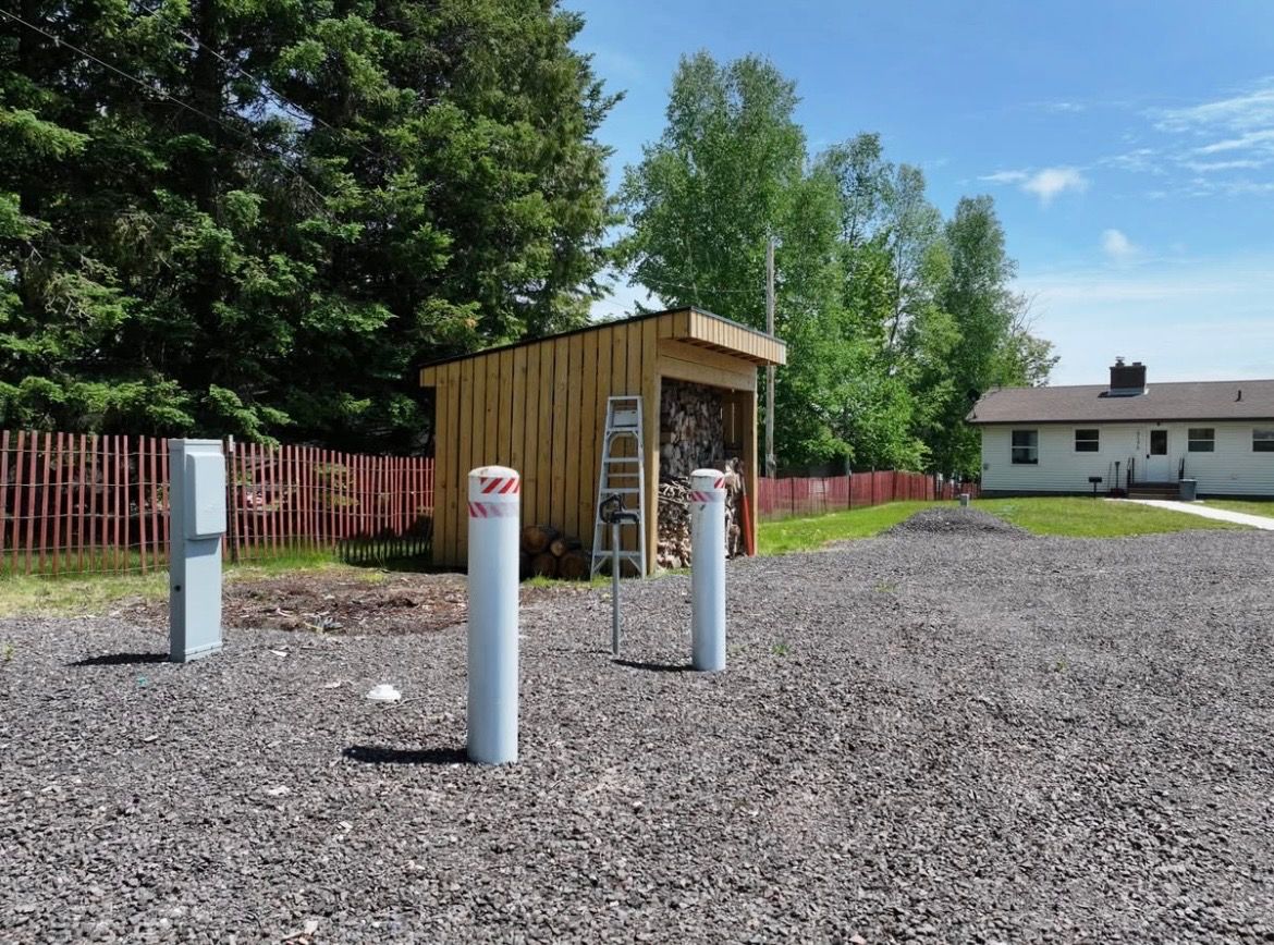 A small wooden structure with a ladder, a fenced area, and a building in the background.