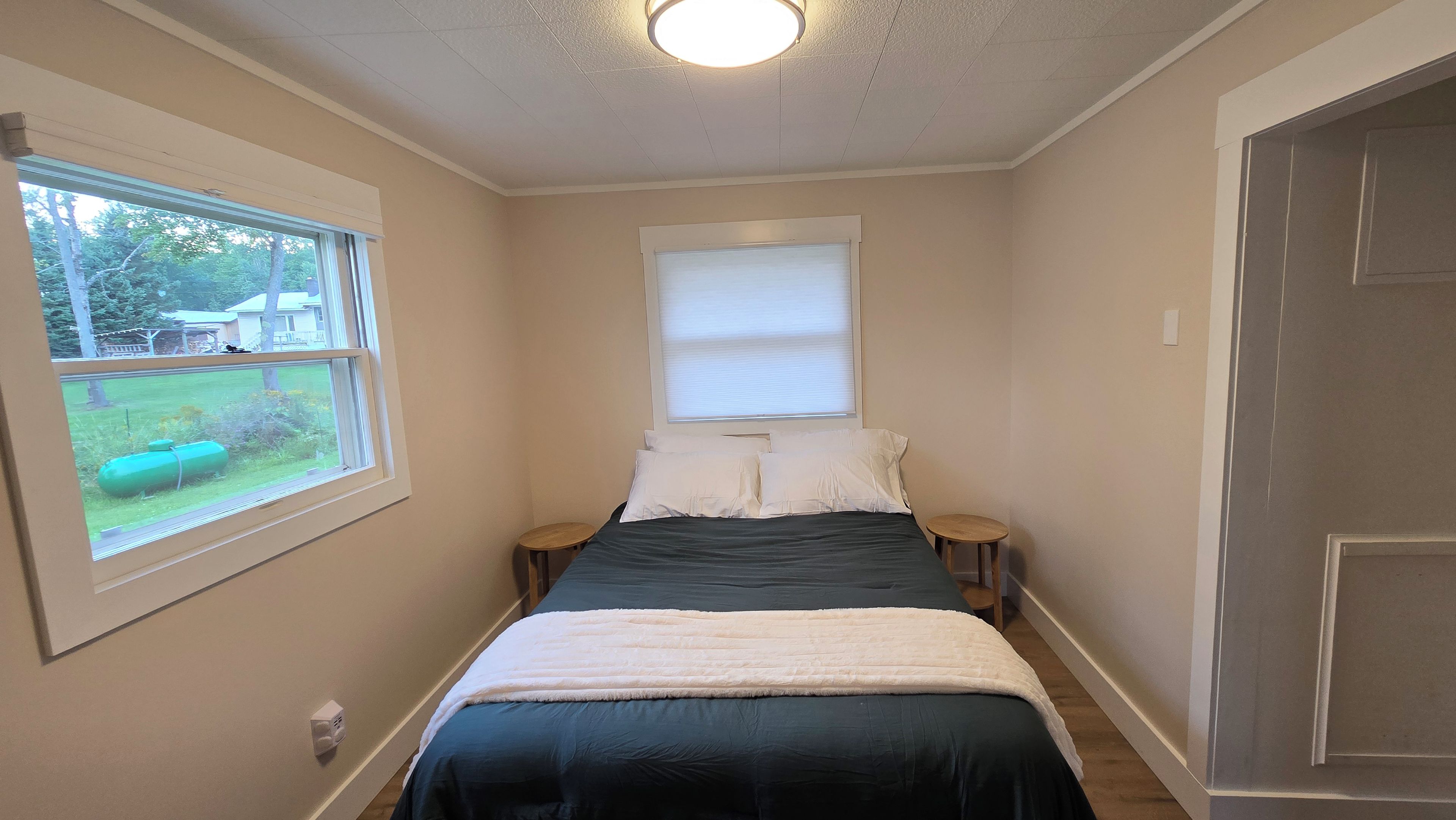 A bedroom with a bed, two bedside tables, a window, and a door.