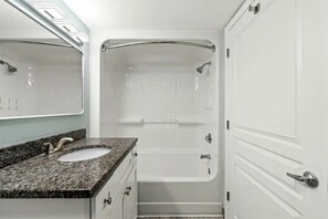 A bathroom with a granite countertop sink, a bathtub, and a mirror. - Designer Oceanfront 1BR at Bay Watch (North Myrtle Beach)
