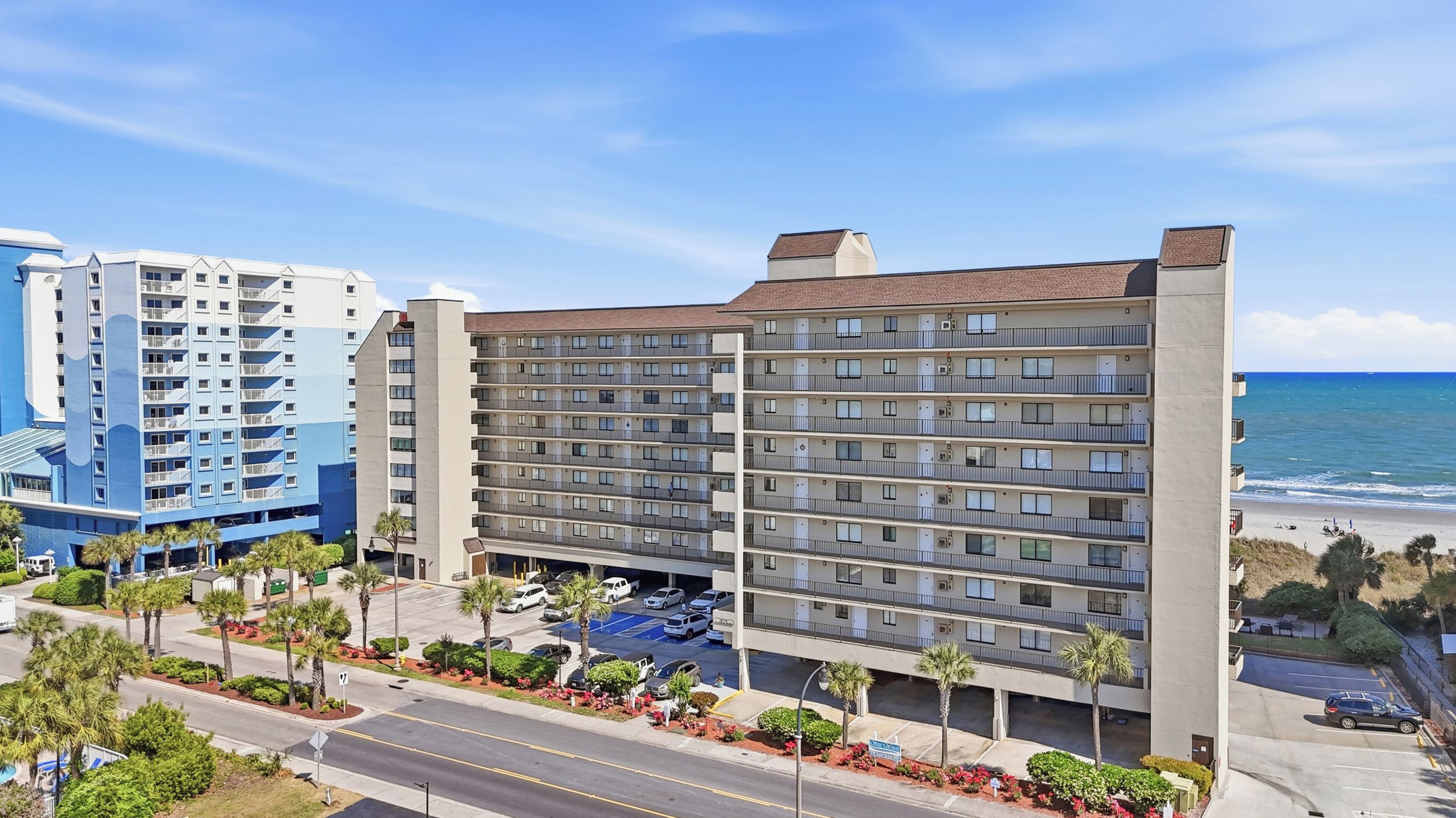 A multi-story hotel with a parking lot and a view of the ocean.
