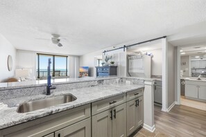A modern kitchen with granite countertops, a built-in sink, and light gray cabinetry. - Wake Up to the Waves | Sea Winds 3BR (North Myrtle Beach)