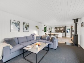 A modern living room with a grey sofa, a coffee table with a magazine and fruit, and a kitchen in the background. - "Hubert" - 450m to the fjord by Interhome (Vemb)