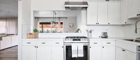 Una cocina moderna con armarios blancos, horno de acero inoxidable y ventana con vista a un paisaje urbano.