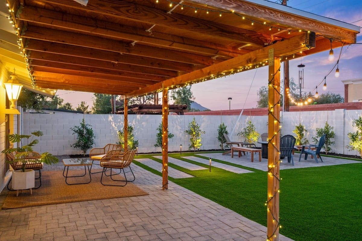 A covered patio area with seating, string lights, and a grassy lawn.