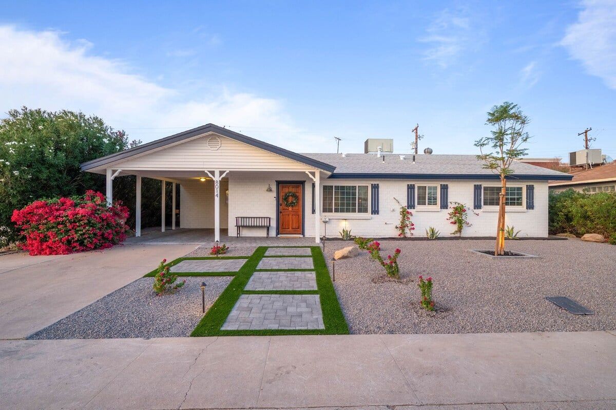 A two-story house with a covered porch, a front door with a wreath, and a gravel driveway with a stone pathway.
