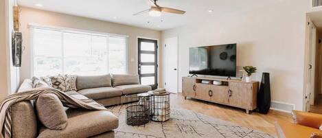 Un salon comprenant un canapé, un téléviseur, un meuble et un ventilateur de plafond.