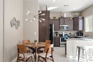 A modern kitchen with a central island, dark cabinets, and a dining area with wooden chairs and a round table. - Mesa Country Club Townhome 🌵⛳ Heated Pool, Jacuzzi & Gym Near Sloan Park (Mesa)