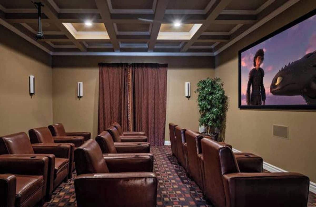 A movie theater with leather recliner seating, a large screen, and a patterned carpet.