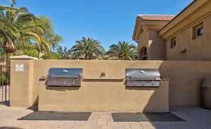 An outdoor barbecue area with two grills, a wall, and palm trees in the background. - Mesa Country Club Townhome 🌵⛳ Heated Pool, Jacuzzi & Gym Near Sloan Park (Mesa)