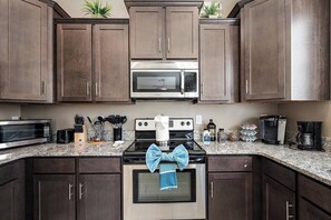 A kitchen with dark wooden cabinets, a stainless steel microwave, a gas stove, and a blue towel tied around the oven handle. - Mesa Country Club Townhome 🌵⛳ Heated Pool, Jacuzzi & Gym Near Sloan Park (Mesa)