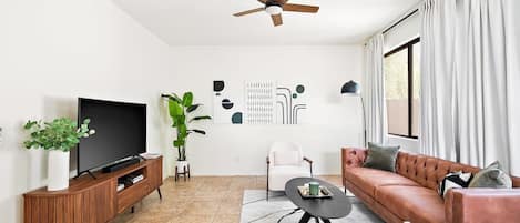 Un salon moderne avec un téléviseur à écran plat, un ventilateur de plafond, un canapé, une table basse et une plante en pot.