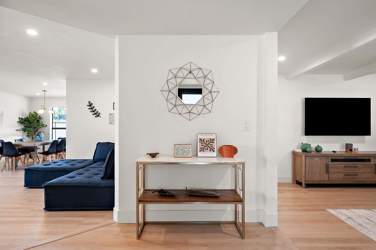 Een moderne woonkamer met een hoekbank, een salontafel, een aan de muur bevestigde televisie en een decoratieve spiegel.
