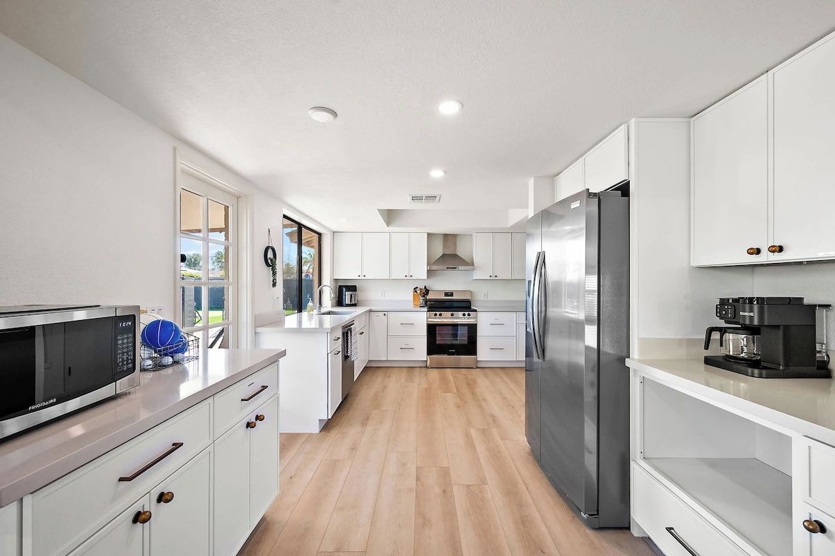 A modern kitchen with white cabinetry, stainless steel appliances, and a wooden floor.