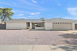 A single-story house with a garage, a driveway, and a gravel front yard. - Mesa Enchanted Forest 🌵⛳ Heated Pool, Hot Tub & Putting Green Near Sloan Park (Mesa)