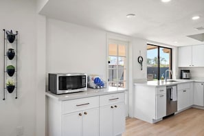 A modern kitchen with white cabinetry, a microwave, a sink, and a window with a view. - Mesa Enchanted Forest 🌵⛳ Heated Pool, Hot Tub & Putting Green Near Sloan Park (Mesa)