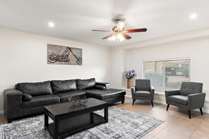 A living room with a black leather sofa, two grey armchairs, a black coffee table, a ceiling fan, and a window with blinds. - Scottsdale Monterosa 🌵⛳ Private Pool, Putting Green Near Old Town Scottsdale (Scottsdale)