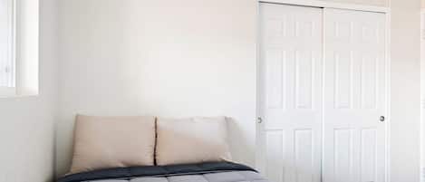 A bedroom with a bed, two pillows, a white door, and a window.