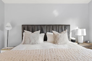 Ein Bett mit dunklem Kopfteil, weißer Bettwäsche und einer grob gewebten Decke.