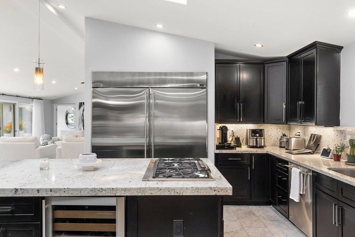 A modern kitchen with a stainless steel refrigerator, dark cabinets, and a granite countertop.