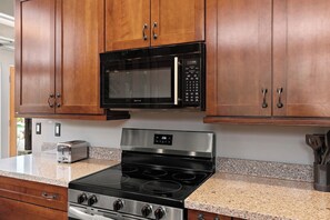 A kitchen with wooden cabinets, a black microwave, a stainless steel stove, and a granite countertop. - Scottsdale Hearn Hideaway 🌵⛳ Heated Pool, Jacuzzi & Kiva Fireplace (Scottsdale)
