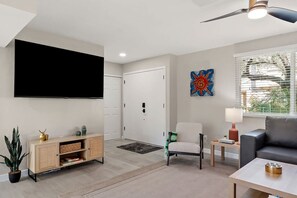 A living room with a flat-screen TV, a sofa, a coffee table, a cabinet, and a door. - Scottsdale Miller Townhome 🌵⛳ Walk to Old Town, Gated Pool & Firepit (Scottsdale)