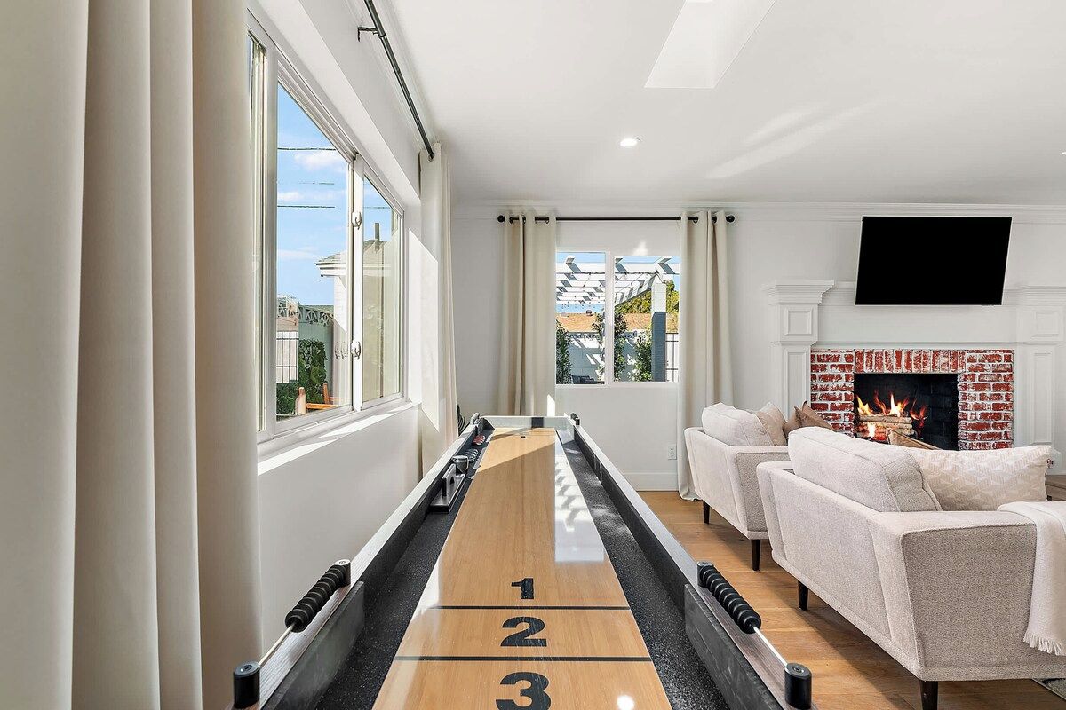 Un salon moderne avec une table de jeu de «shuffleboard», une cheminée et un téléviseur fixé au mur.